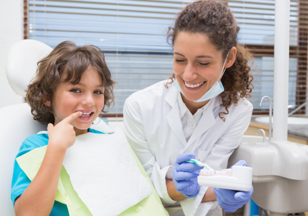 dentist showing child how to brush while he points to his teeth
