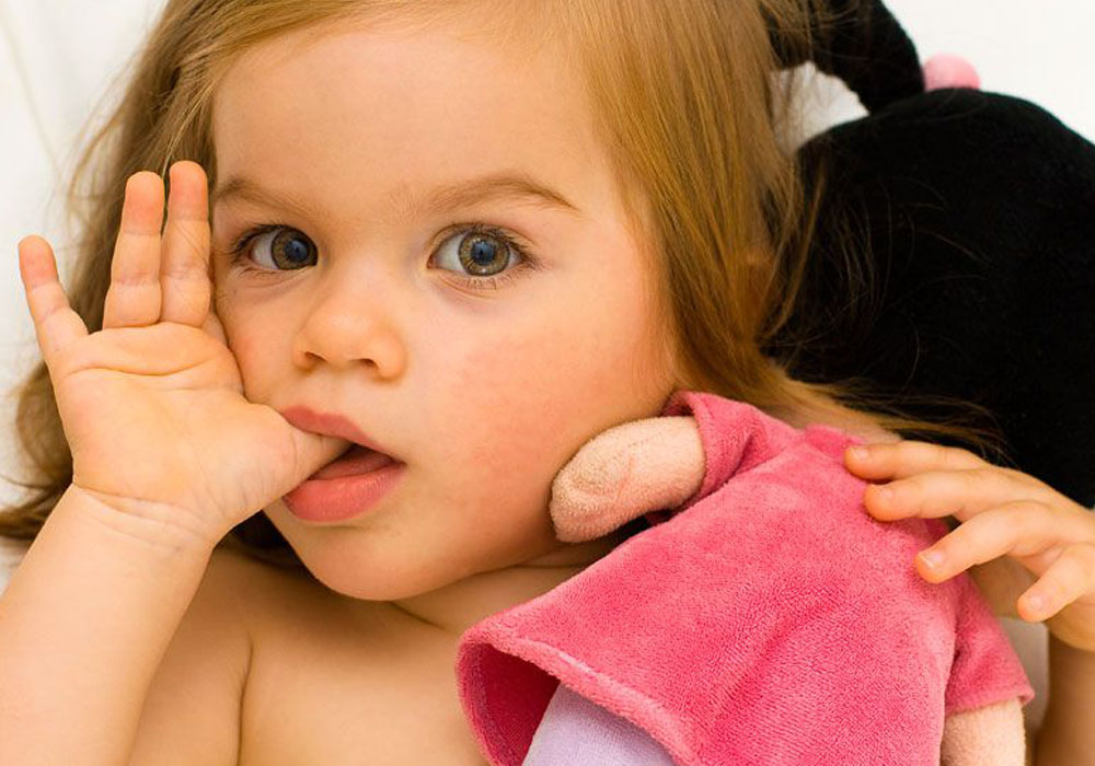 toddler holding a doll while sucking her thumb